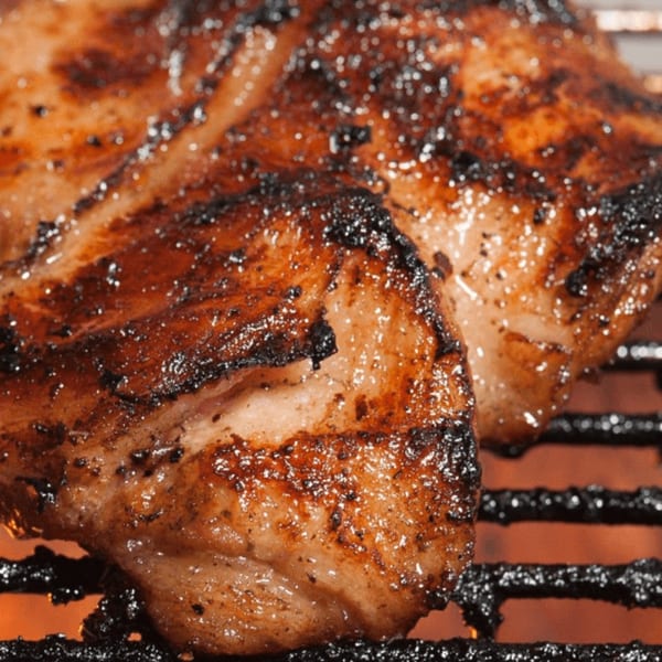 Close-up of two pieces of Alice's Bar-B-Que meat sizzling on a grill over glowing coals.