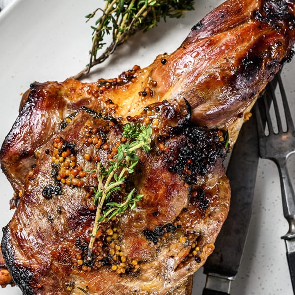 Close-up of a glistening, grilled Alice's Bar-B-Que meat cut with herbs and mustard seeds.