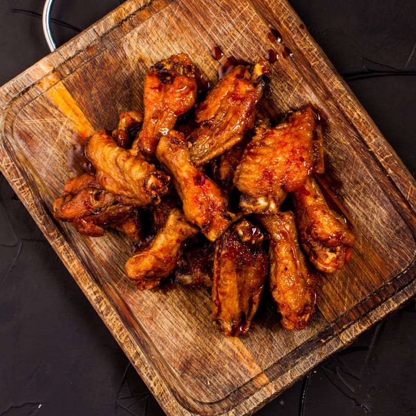 Alice's Bar-B-Que LLC's sticky, glazed BBQ chicken wings on a rustic wooden cutting board.